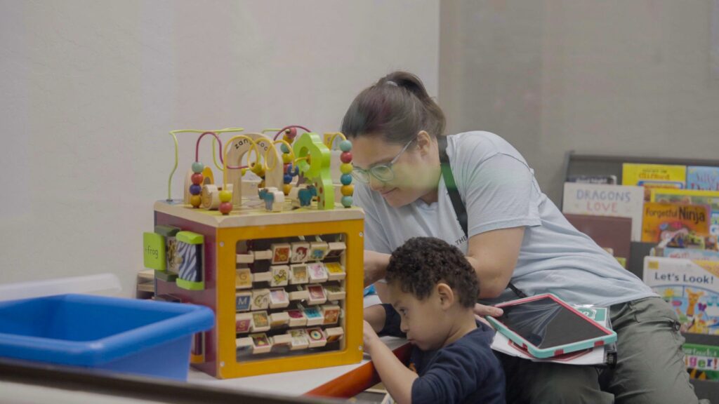 Treetop ABA therapist helping a child use a learning tablet near educational toys