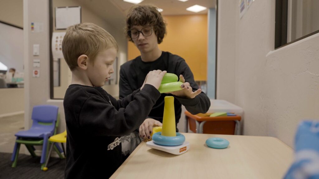 Child placing rings on a stacking toy with therapist guidance at Treetop ABA