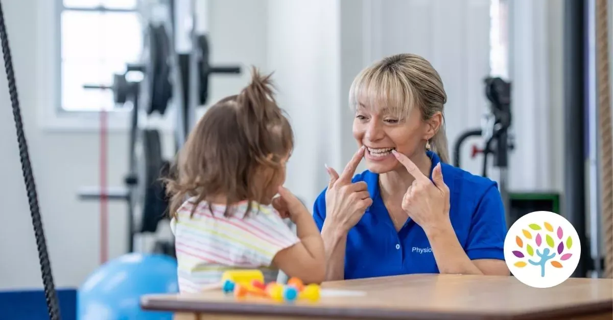 Therapist and child smiling across a table during a playful session in a gym-like therapy room
