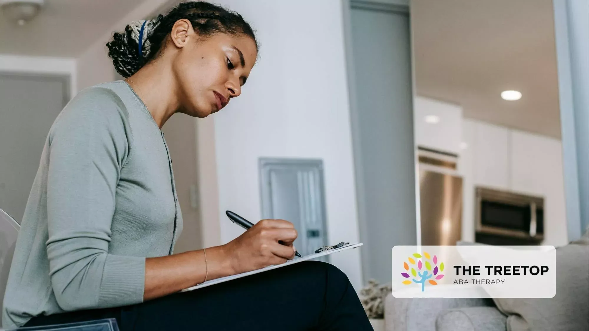 Woman writing on a clipboard in a bright room with The Treetop logo on a box in the background