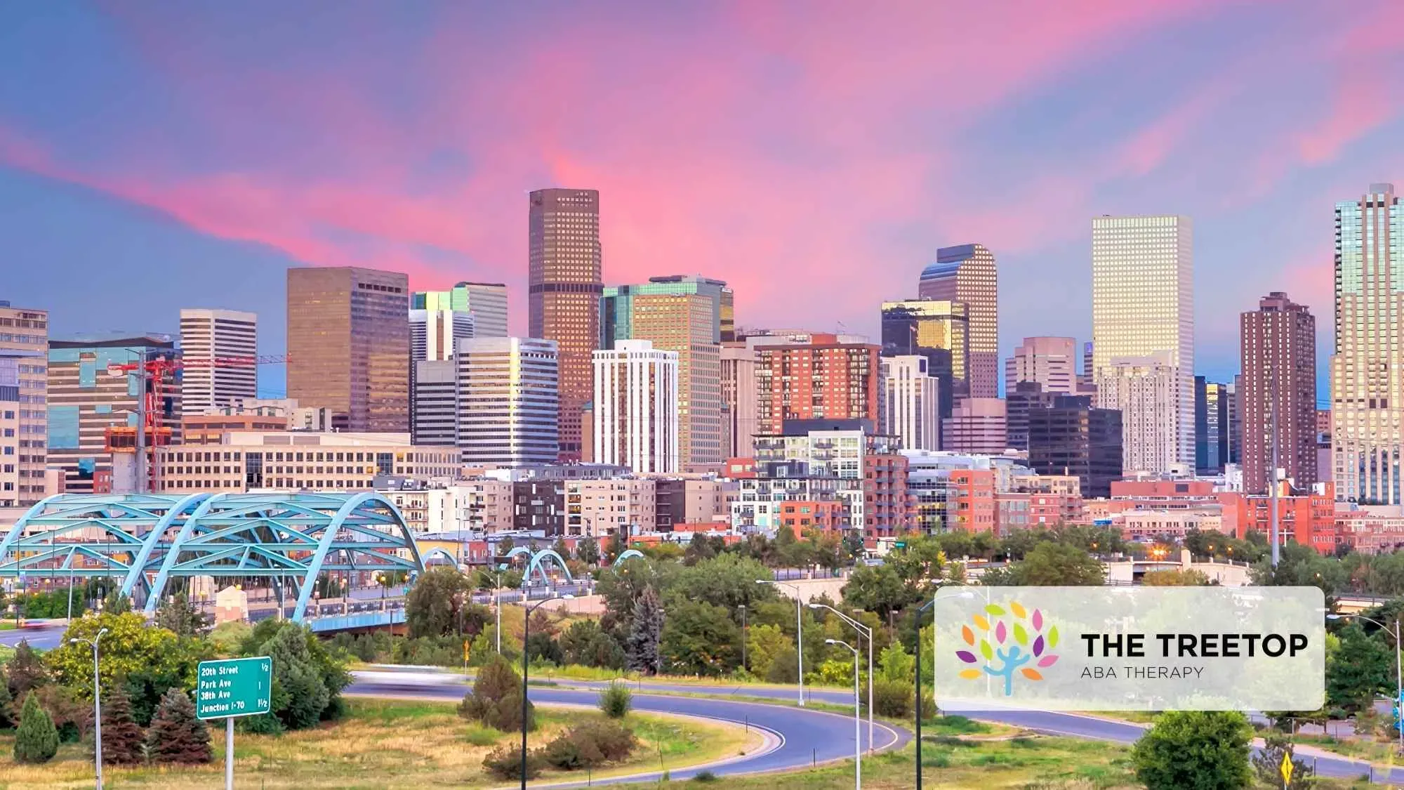 City skyline at sunset with pink sky, modern buildings, and a sign reading “The Treetop” in the foreground.