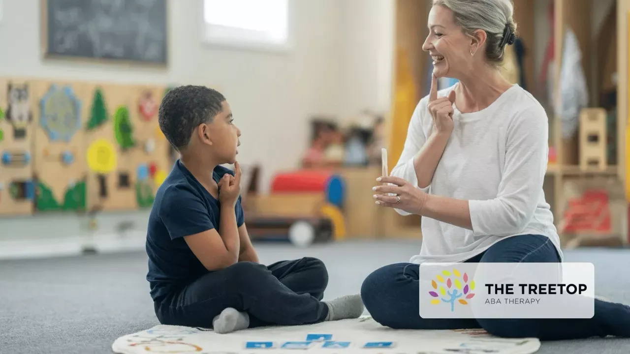Teacher and child sitting on a carpet, smiling and talking in a bright classroom.