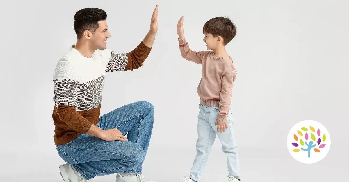 Man and child facing each other, giving a high five in a bright studio setting.