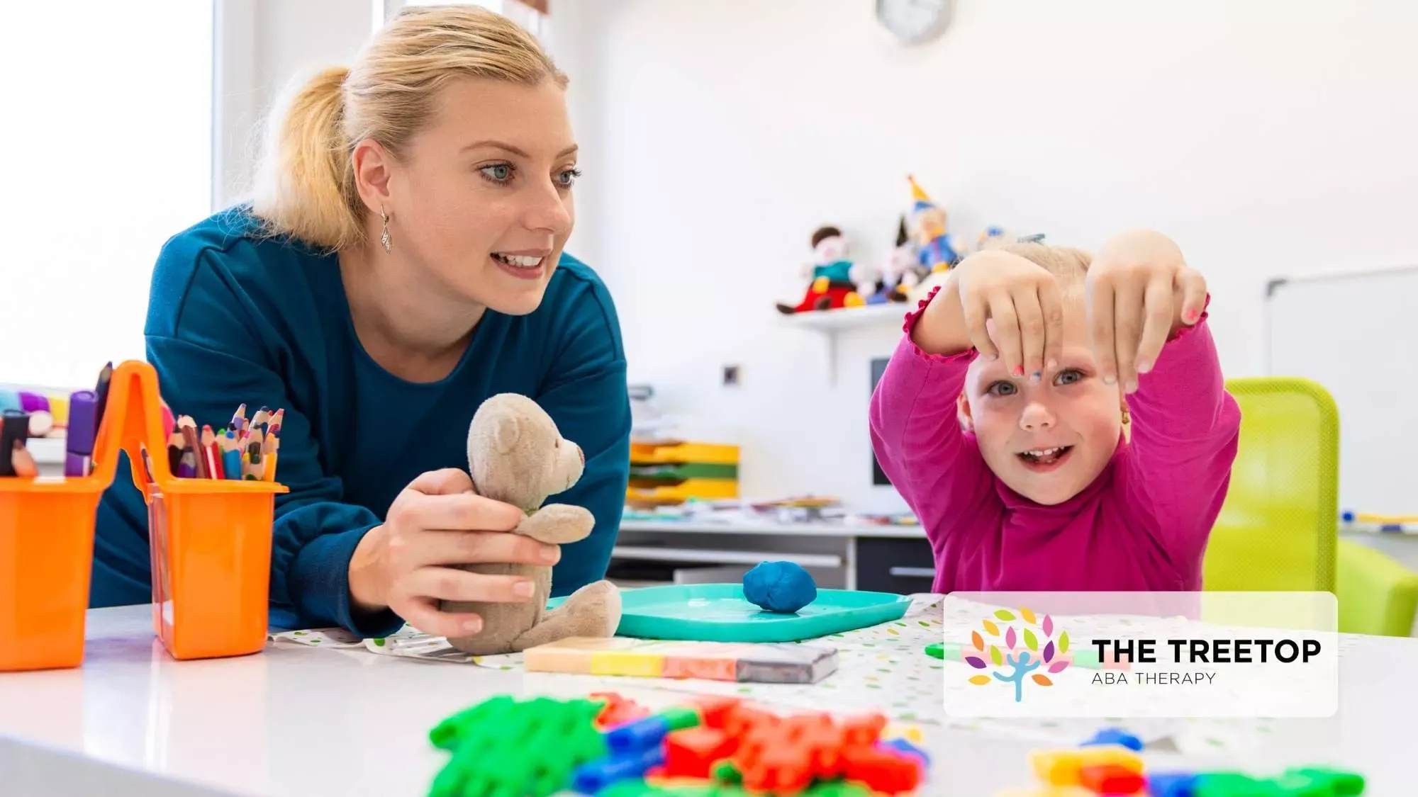 An instructor and a child interact with a small toy and colorful building blocks in a classroom setting.