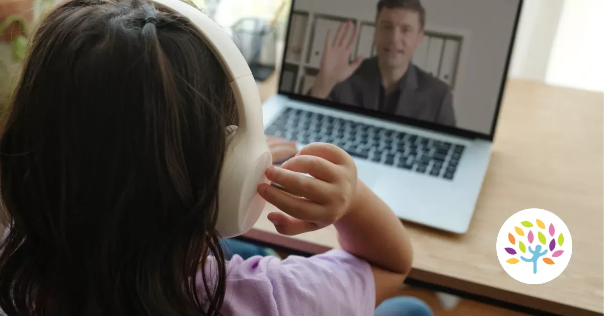 A person wearing headphones participates in a video call on a laptop, with a professional visible on screen.