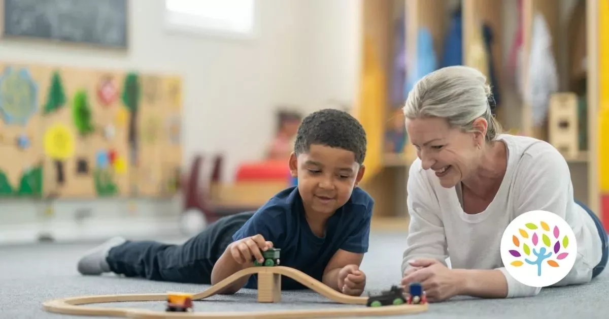 Child and adult on the floor building a wooden bridge toy in a bright classroom